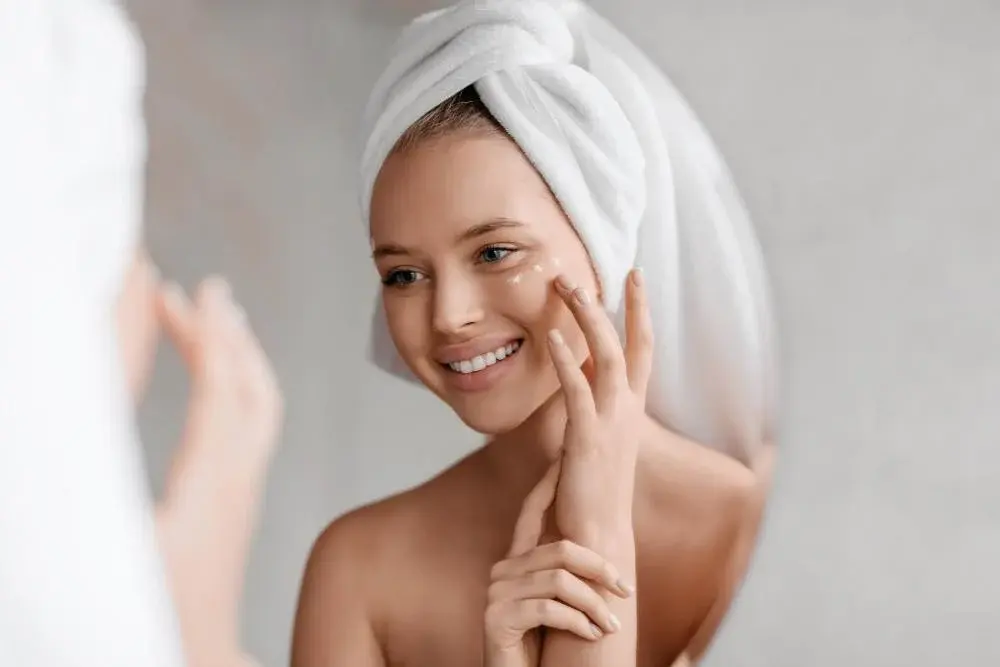 portrait young lady applying nourishing eye cream after shower looking mirror smiling