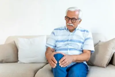 elderly man sitting sofa home touching his painful knee people health care problem concept unhappy senior man suffering from knee ache home 400